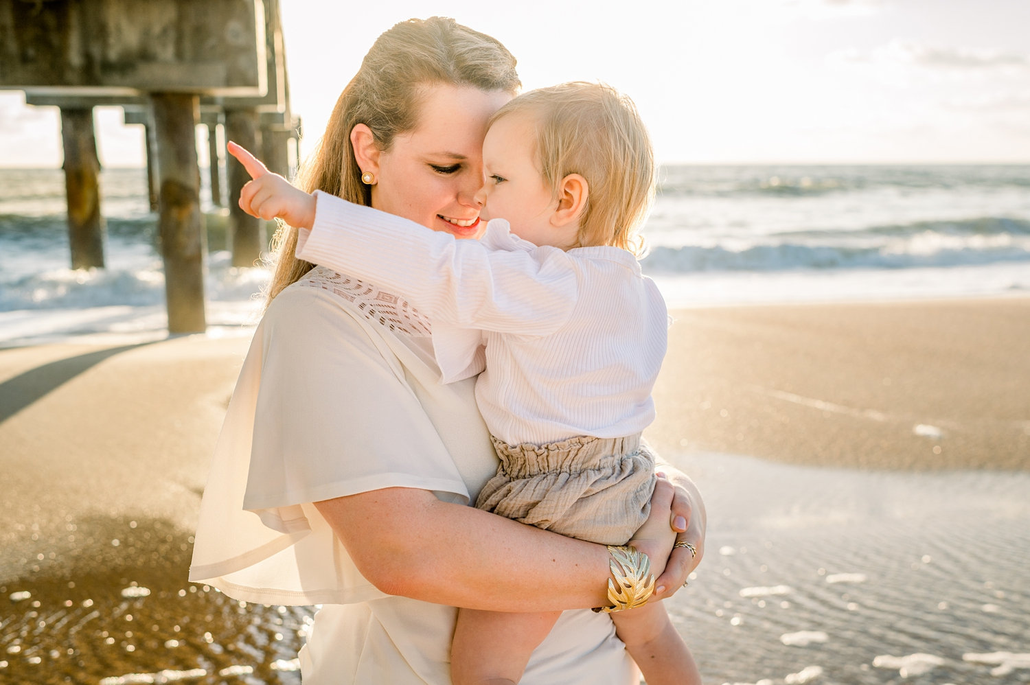 mother smiling down at baby daughter, little girl pointing at the beach, Rya Duncklee