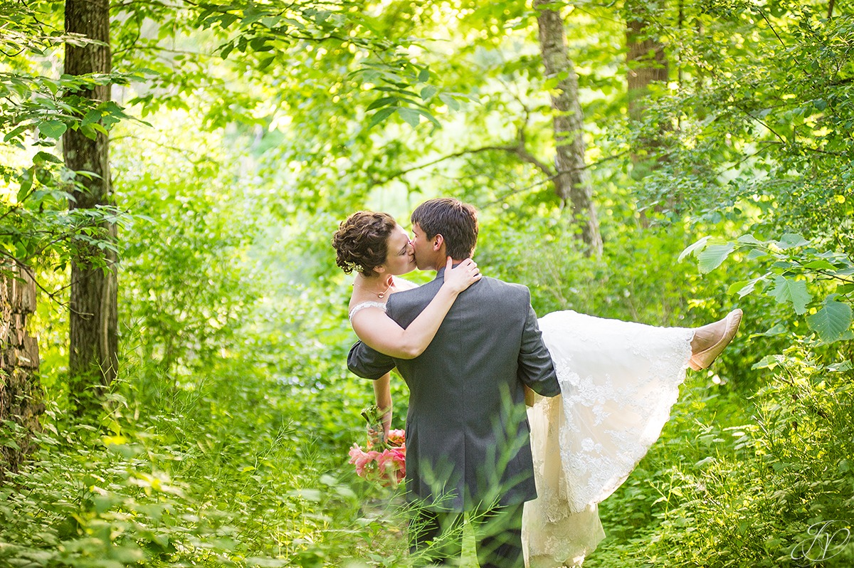 groom carrying bride through the woods