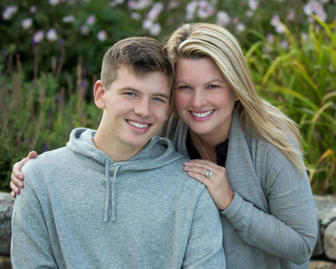 outdoor family portrait of mother and teenaged son by stone wall with flowers