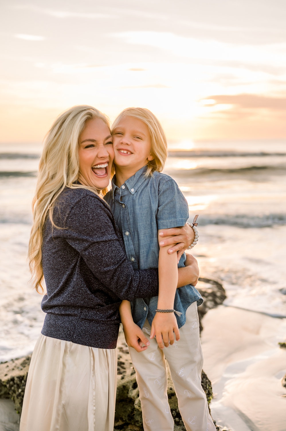 laughing, joyful mom hugging her son, there are coastal rocks and the Atlantic ocean in the background