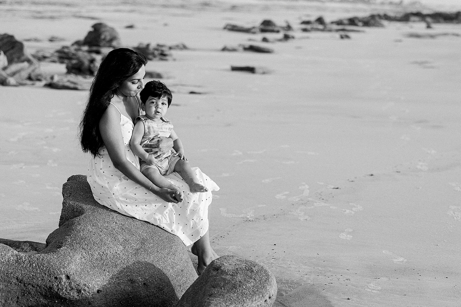 woman and baby sitting on rocks on the beach black and white image