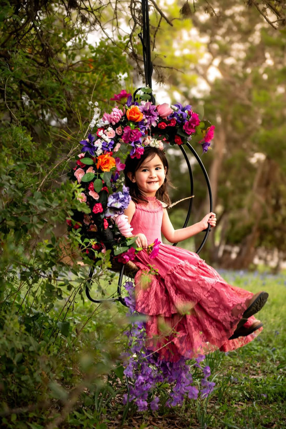 Child portrait on floral swing in garden setting by Austin child portrait photographer Texas Vogue Photography.