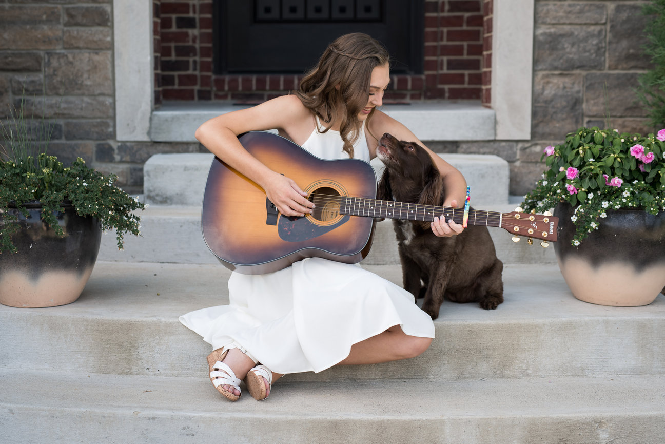 high school graduate girl plays guitar on her front porch with her dog