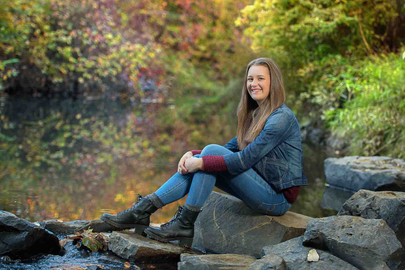Senior girl sitting on rocks along a riverbank in the fall