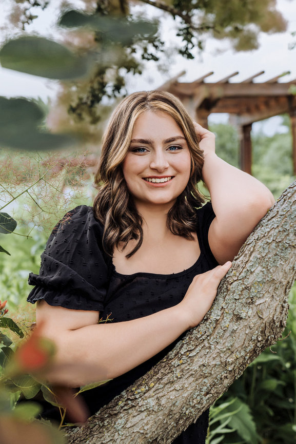 Senior picture of a girl in a black dress leaning on a tree branch in Minneapolis Minnesota