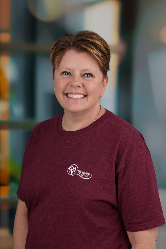 Person smiling in a maroon shirt with a logo, standing against a blurred background.