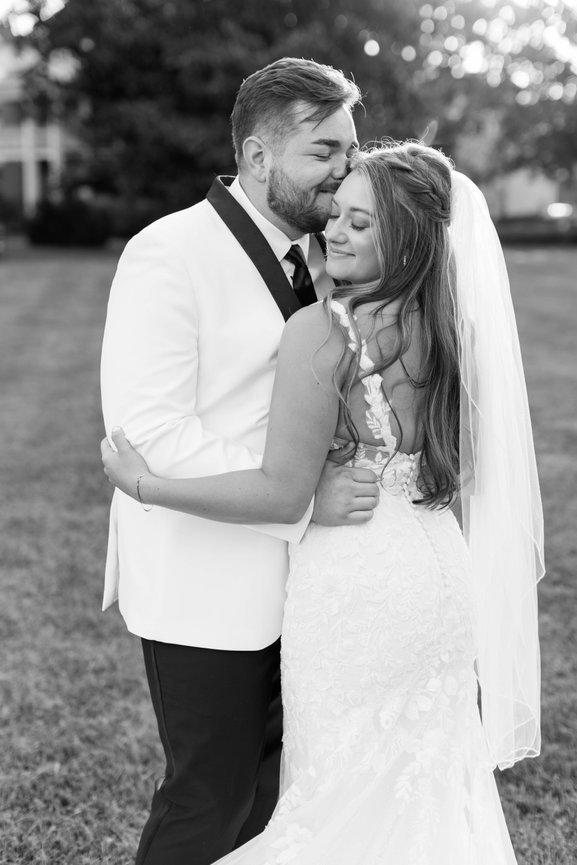 Groom holding brides waist and kissing her temple with her back to the camera to show the back of the dress