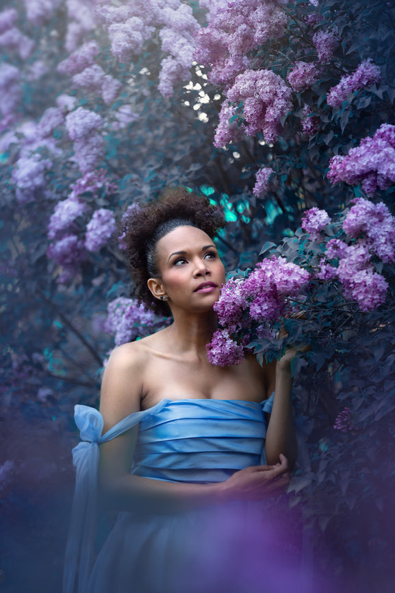 Woman in a blue dress touching lilac flowers