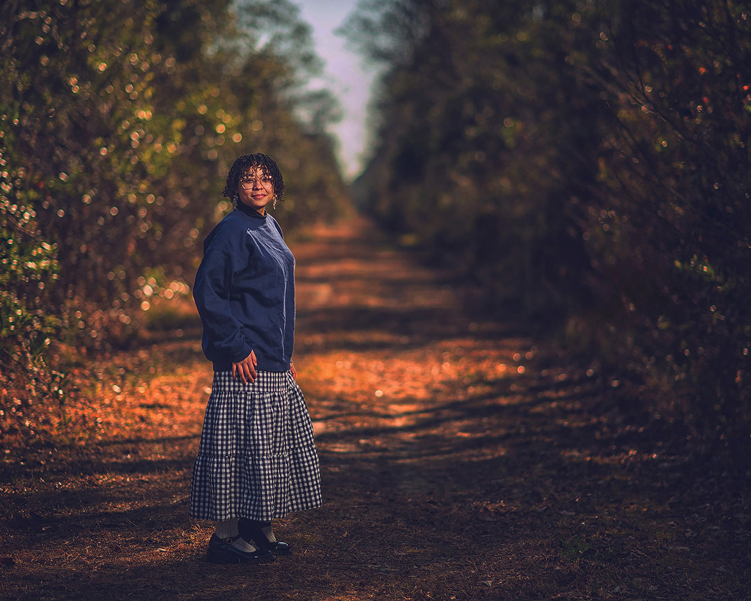 High school senior girl in plaid skirt and sweater on autumn pathway with golden bokeh foliage, fine art Texas environmental senior portrait by Swartz Portraits in Spring TX serving The Woodlands and Conroe