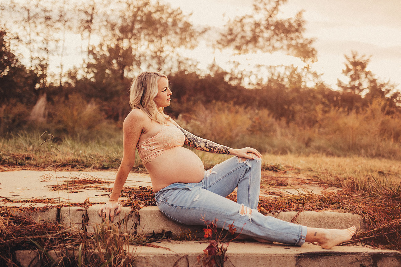 Pregnant woman with tattoo seated outdoors at sunset in a field
