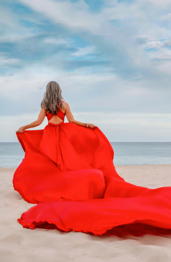 Woman in flowing red flying dress on the beach with a blue-sky background