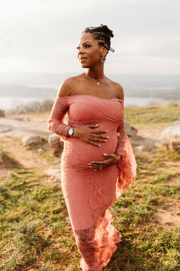 a Black pregnant woman caresses her belly and looks into the light in a Huntsville, Alabama maternity photoshoot