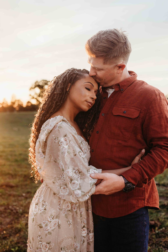 A red-haired man embraces his wife and kisses her forehead in a Huntsville Alabama family photoshoot