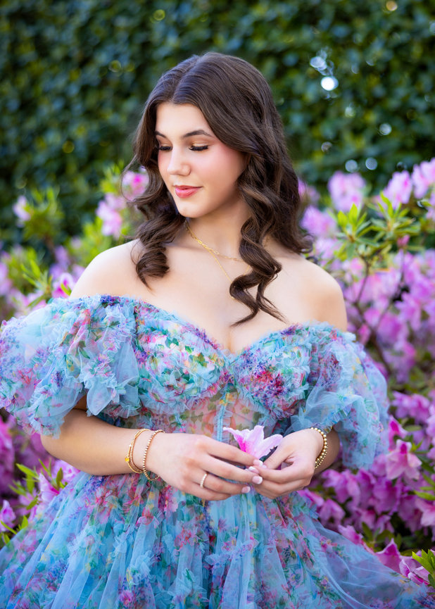 Teenage girl in blue off the shoulder floral dress holding a pink flower.