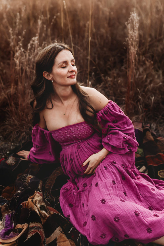 A mother to be in a pink dress relaxes in a field in Stanhope, New Jersey while having maternity photos taken.