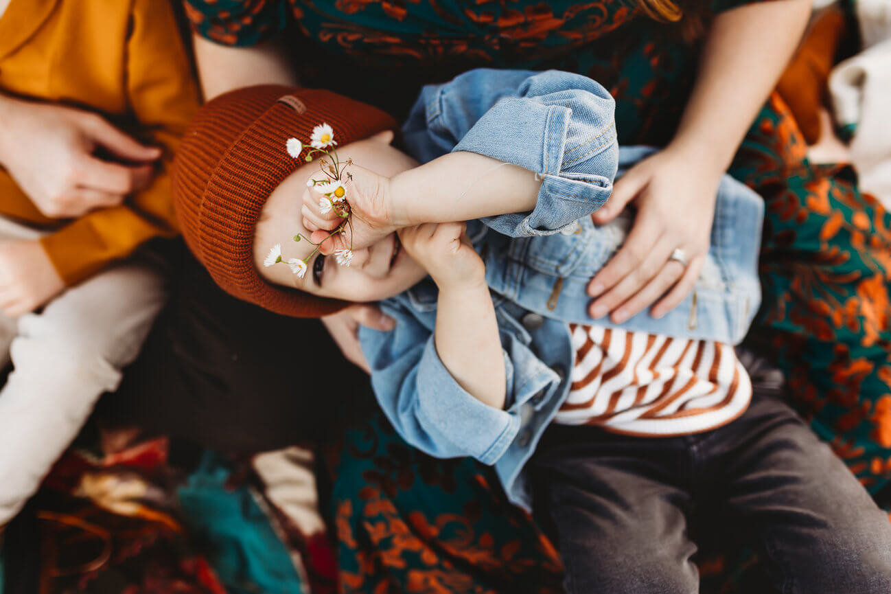 A boy laying in his mothers lap and holding flowers during a New Jersey family photography session at the Central Park of Morris County.
