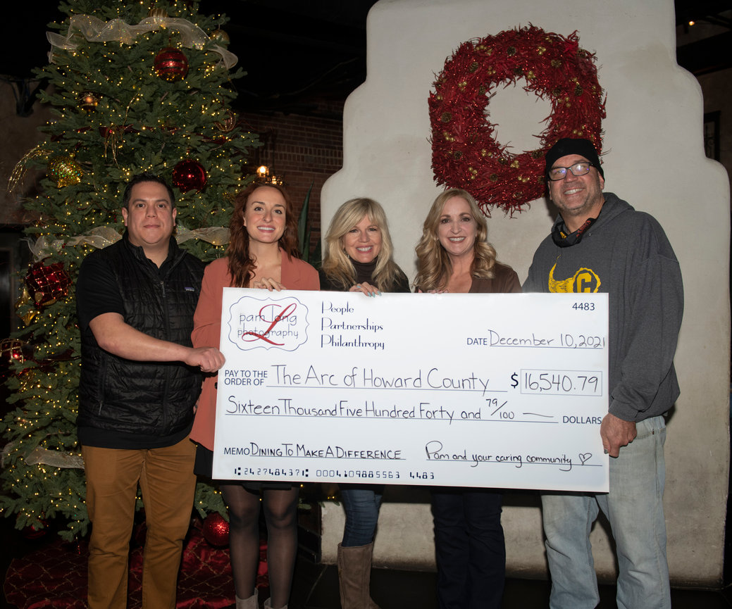 Group of people holding a large check in front of a decorated Christmas wreath.
