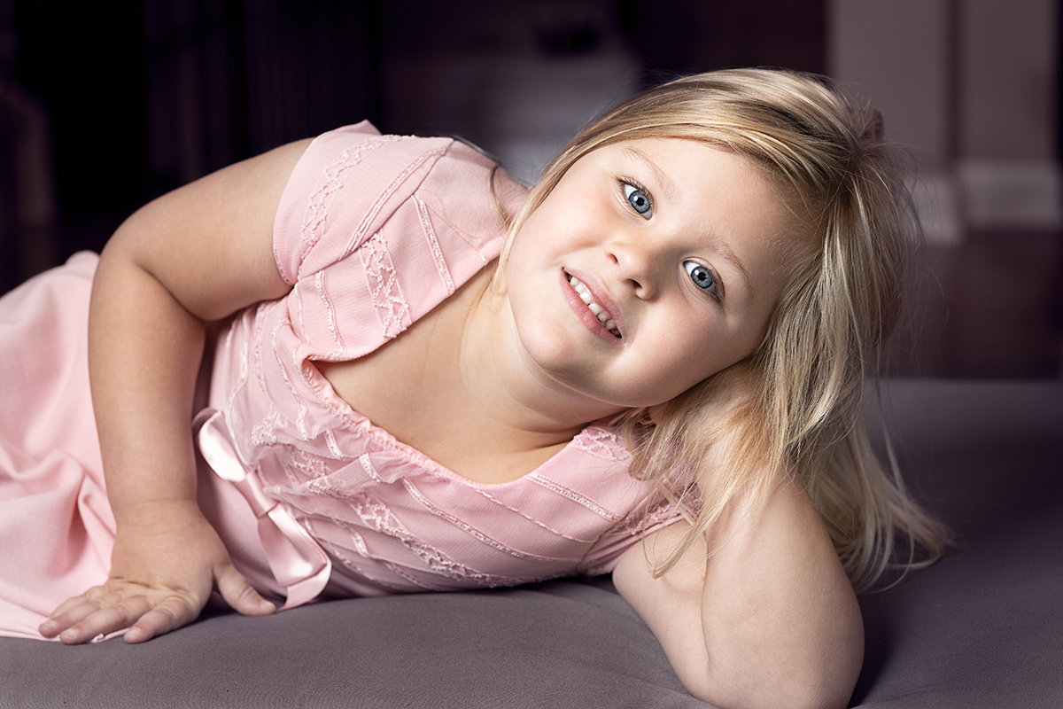 Indoor portrait of a young girl lying on a sofa in Noblesville, Indiana, captured in soft natural-style light with a relaxed and joyful expression