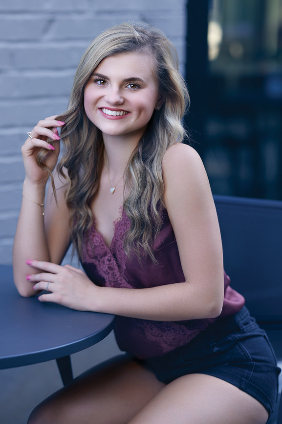High school senior portrait of a young woman smiling outdoors, photographed with natural light and subtle studio lighting for a bright and refined style