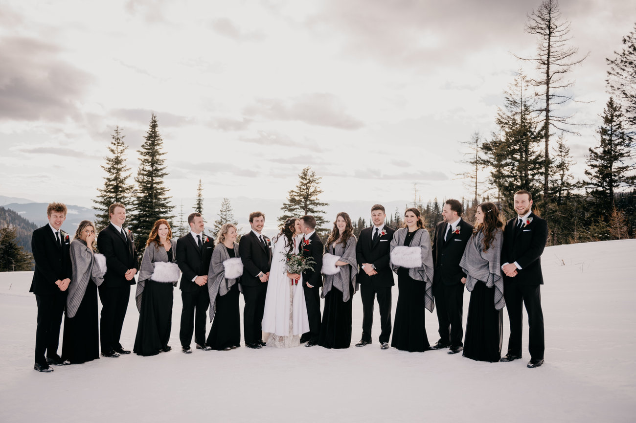 Family group photo: Smiling family gathers for a portrait during a Kelowna wedding, with mountains and vineyards in the background.