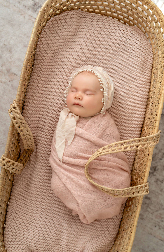 Sleeping newborn wrapped in pink blanket in a woven basket with lace bonnet- San Diego Photography