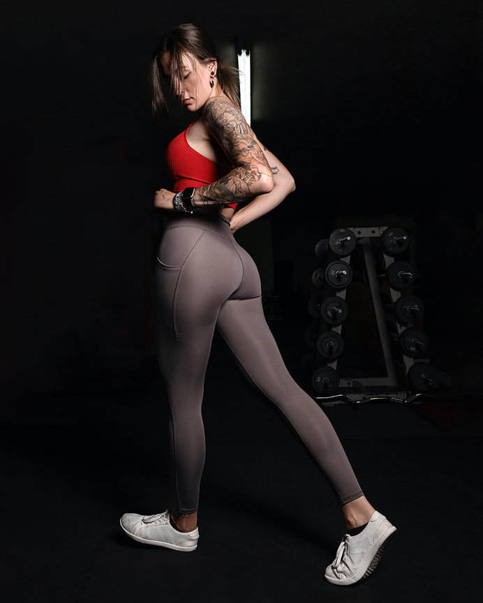 Fitness influencer wearing a red sports top and gray leggings posing confidently in a gym at Rage Fitness in Lehi, Utah. Captured by Tre Nelson Photo, specializing in fitness and personal branding photography.