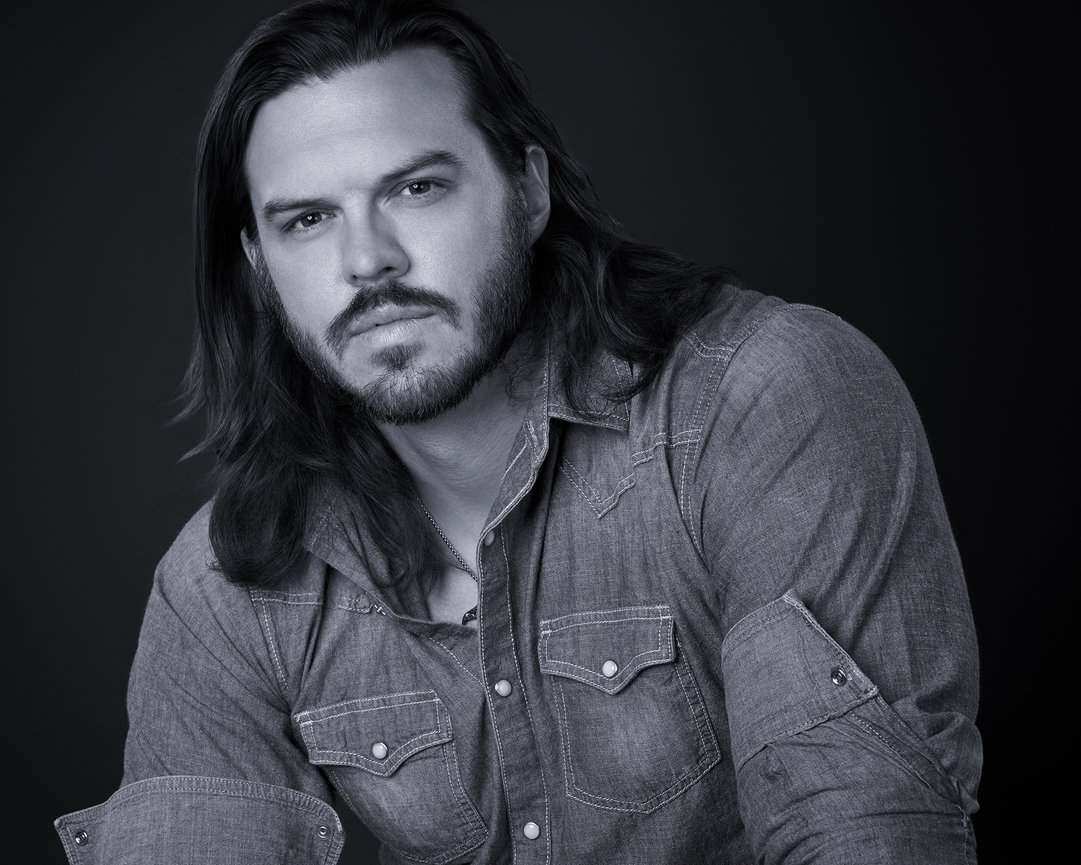 Black and white portrait of a man with long hair and a beard wearing a denim shirt, photographed in Sherman Texas for dramatic and timeless personal branding