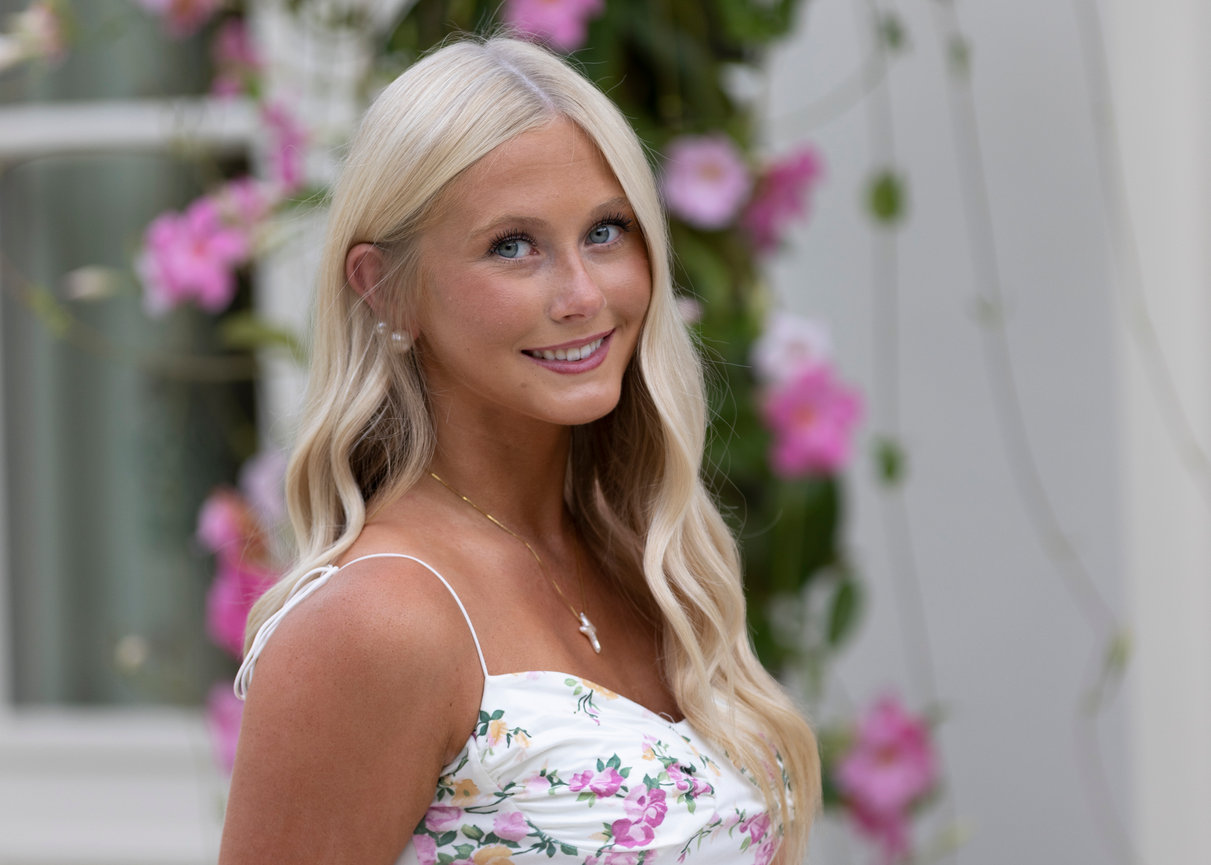 Close-up portrait of a smiling blonde woman with pink flowers in the background.