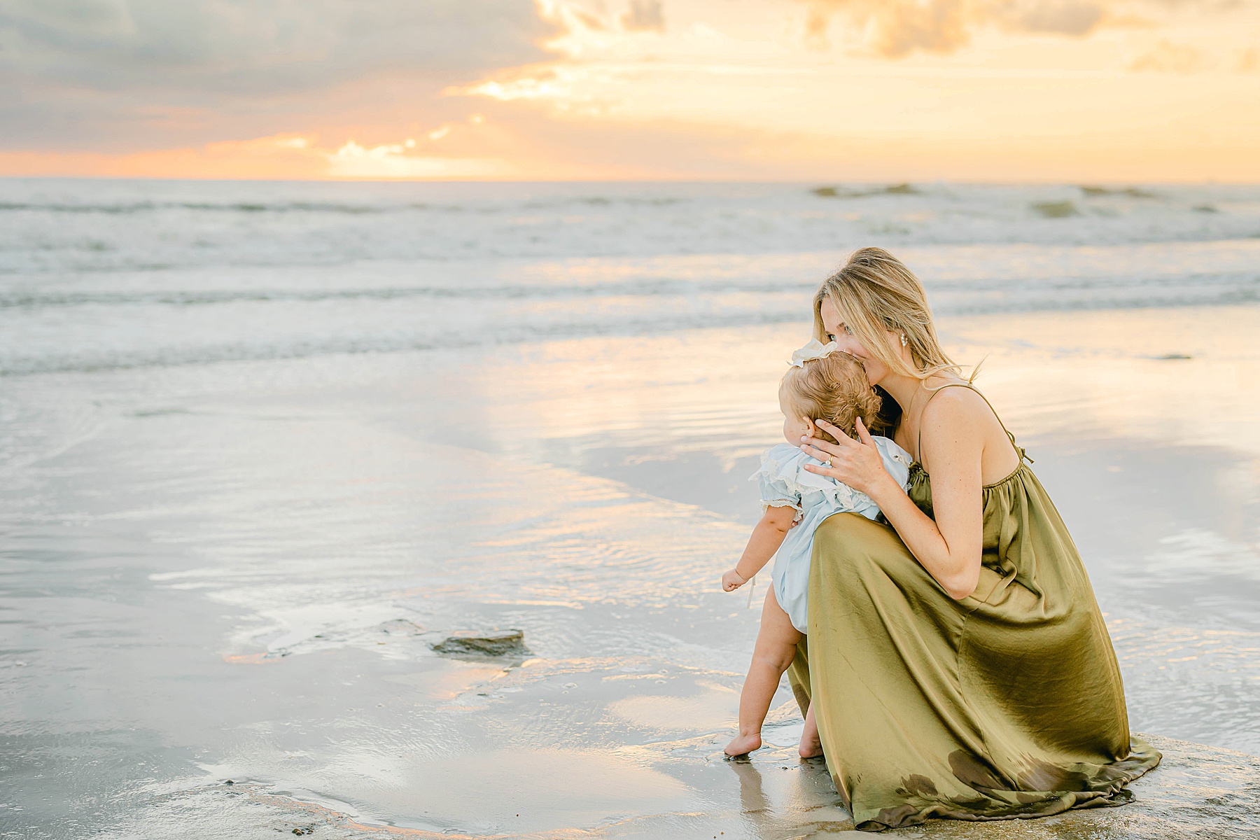 woman and baby standing in the water at the beach at sunrise