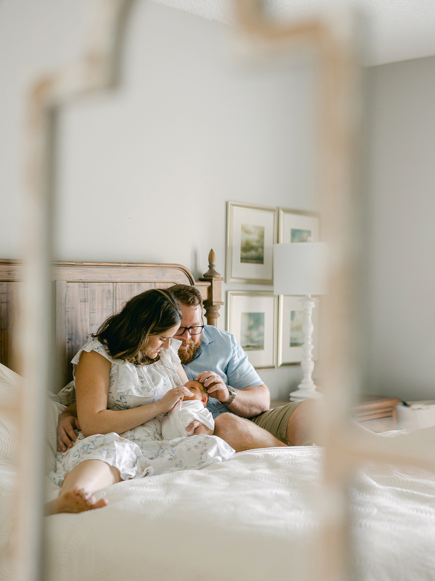 photo of mirror looking at man and woman sitting on bed holding newborn baby