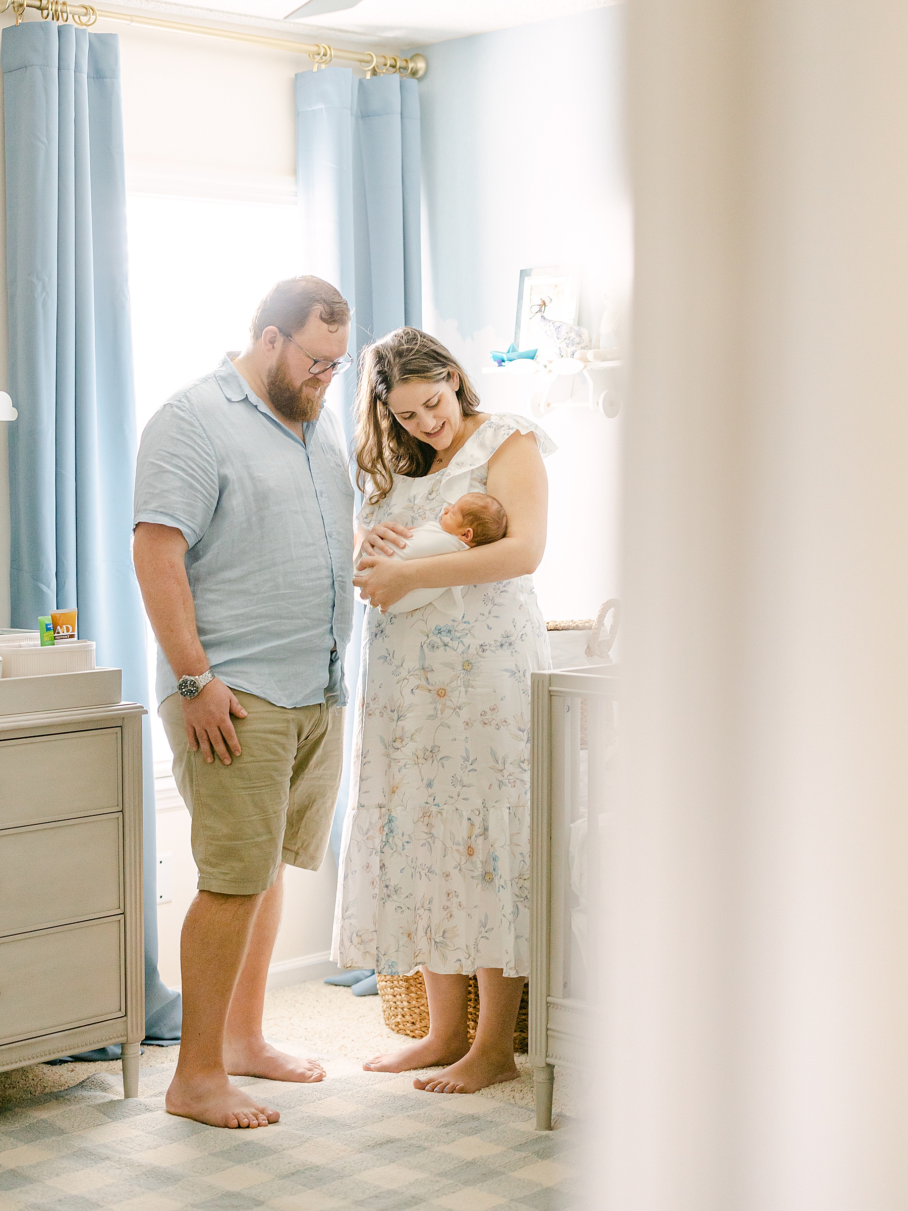 man and woman holding newborn baby boy by window in blue and gold nursery