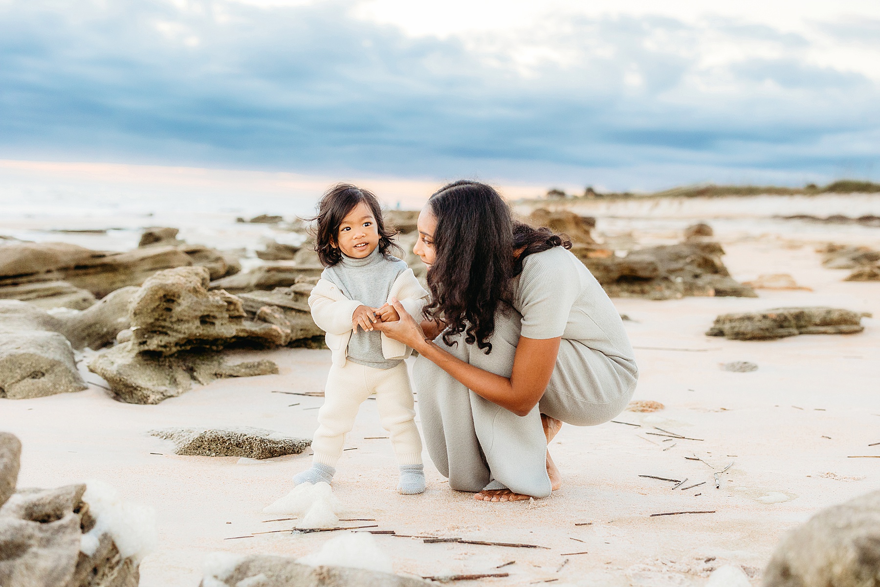 woman smiling kneeling at baby boy on the beach at sunrise
