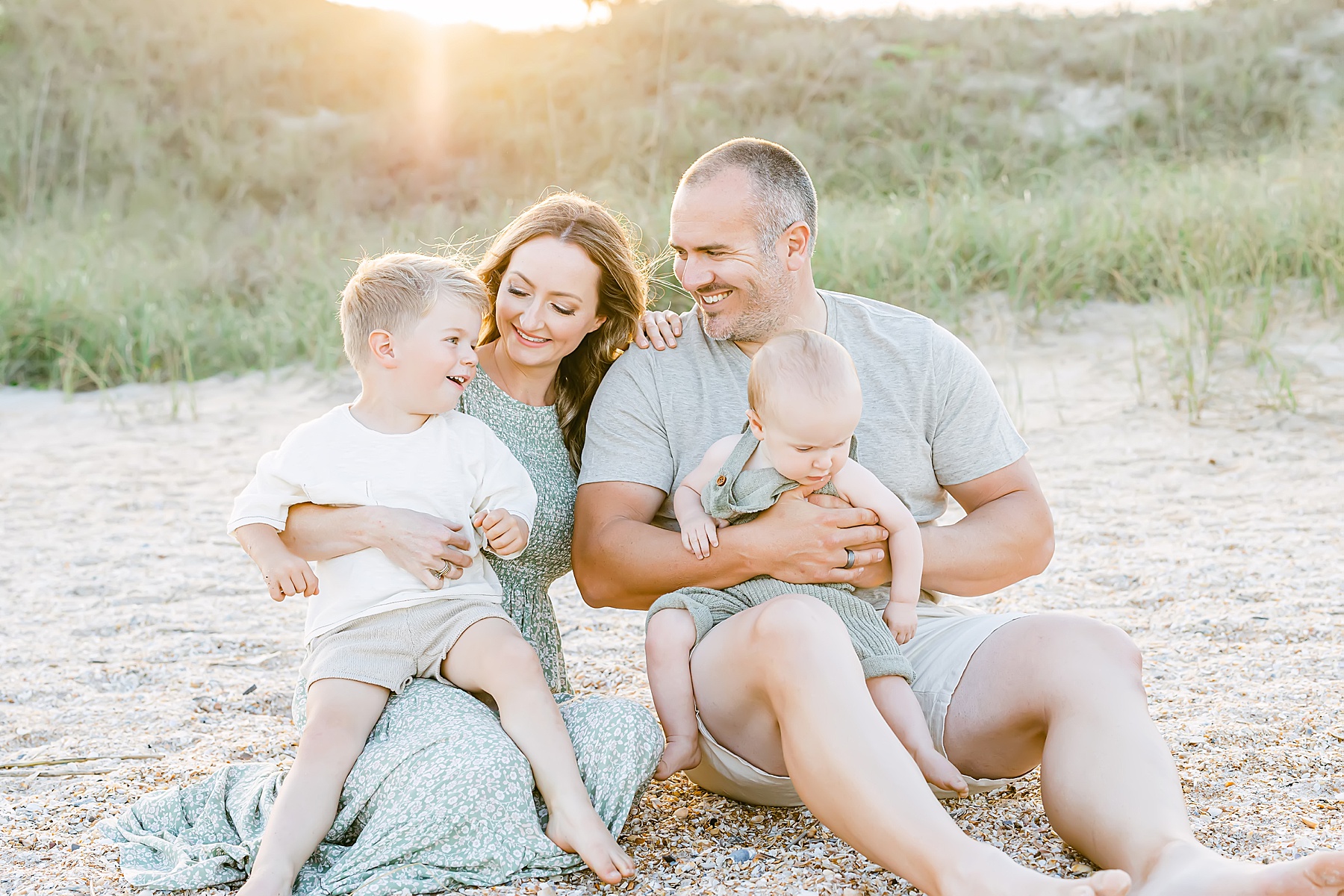 family sitting together on the beach at sunset wearing neutral colors