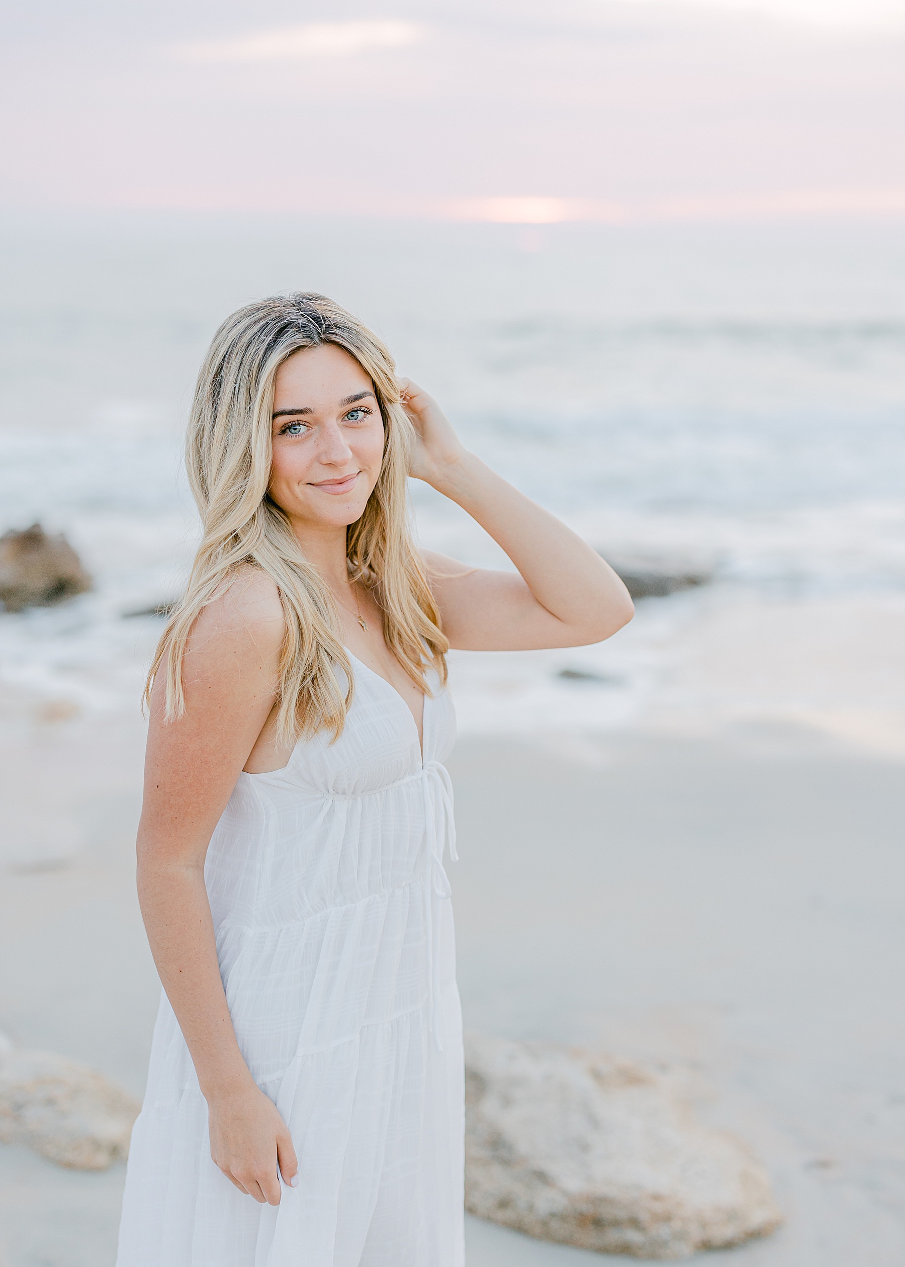 grad senior standing on the beach at sunrise in florida wearing a long white dress