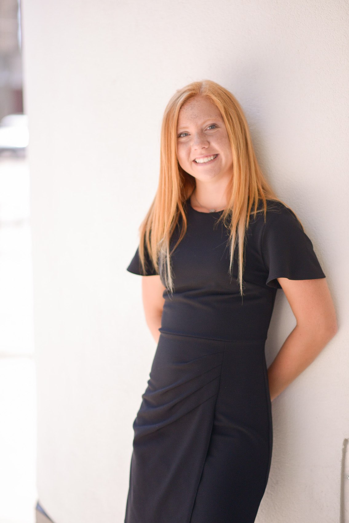 Senior girl in a black dress leaning against a wall in front of The Complex on Park Central East in Springfield, MO. 