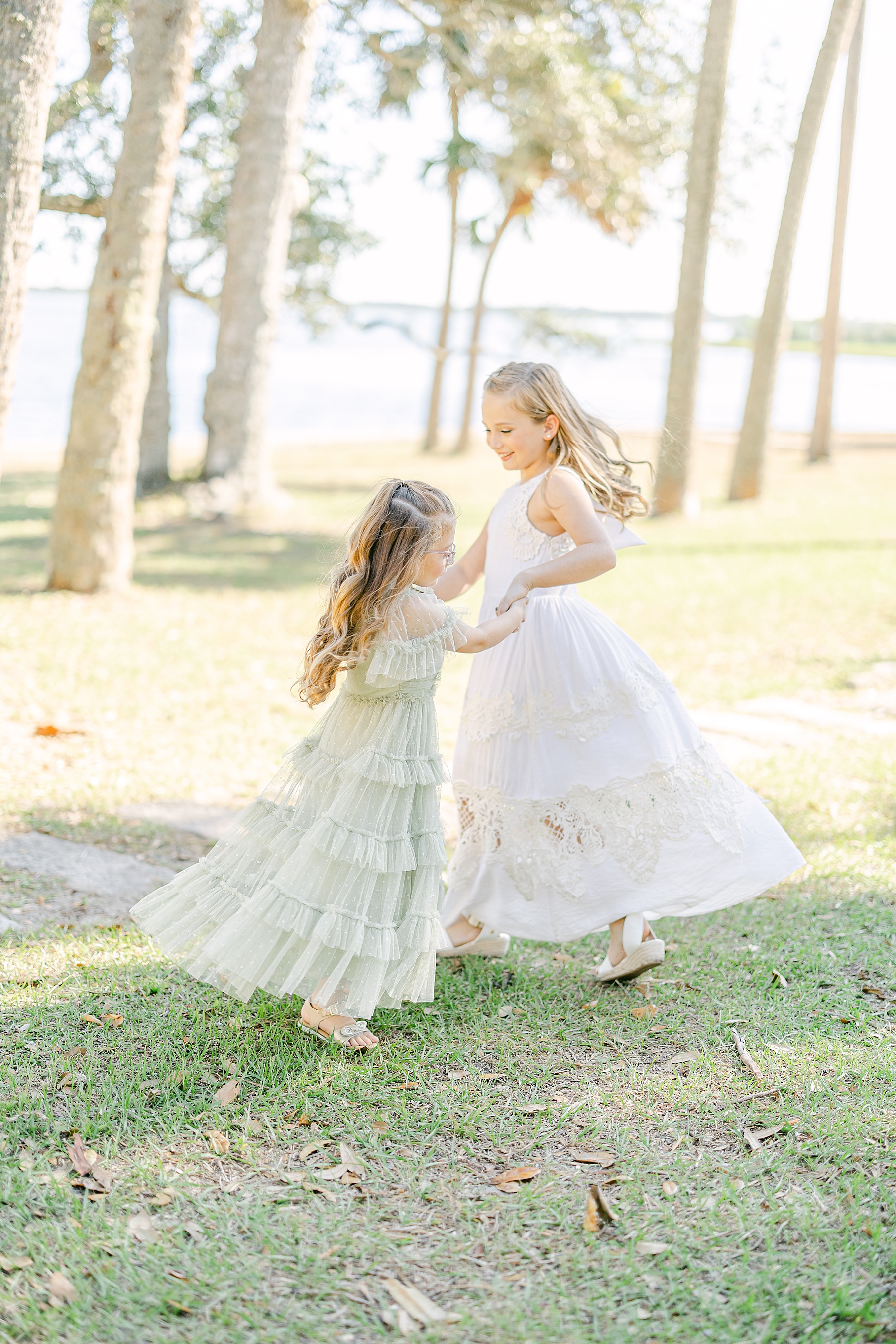 two little girls dressed in white dresses dancing together in the sun at Princess Place Preserve
