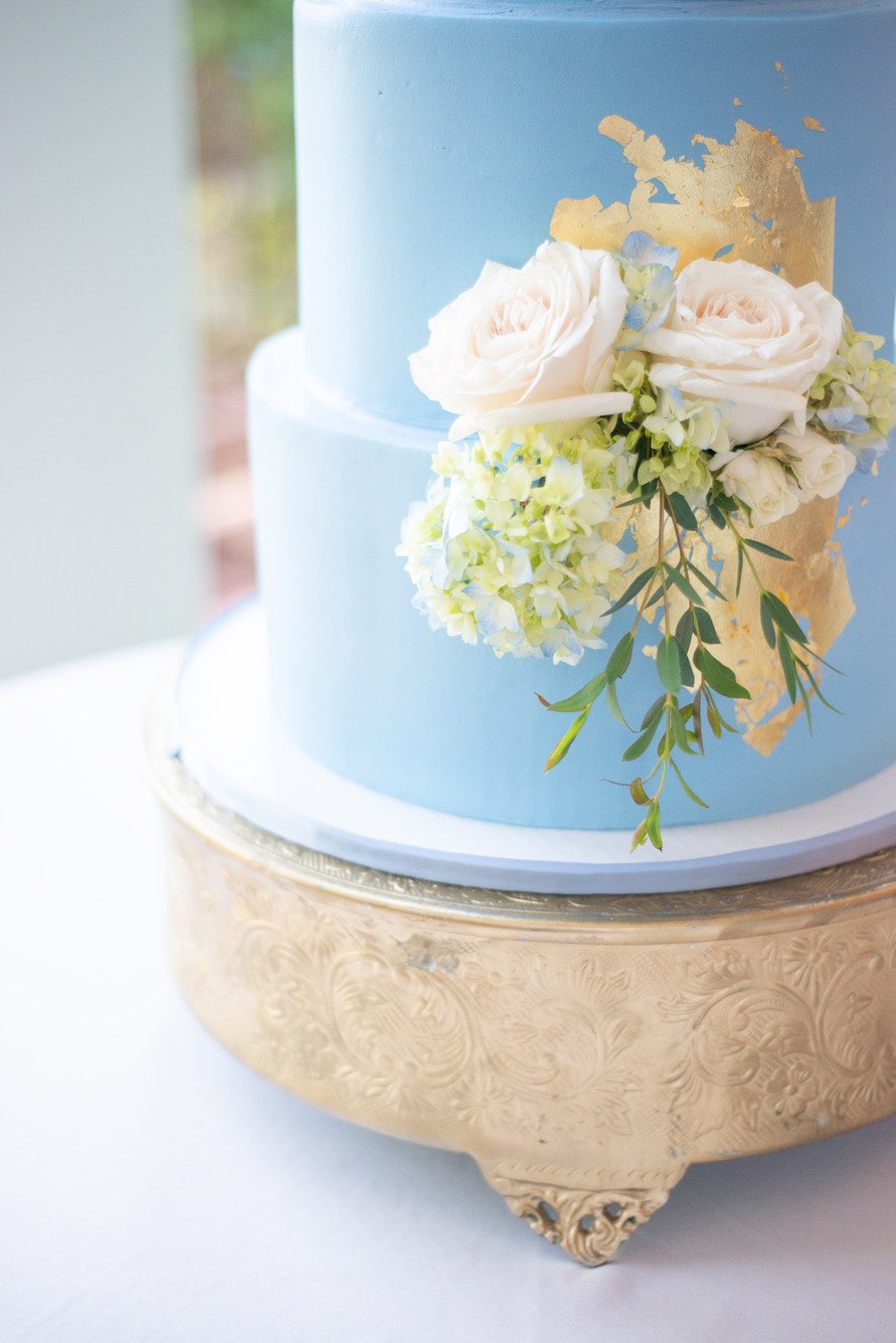Detail shot of gold foil and fresh flowers on a blue cake.