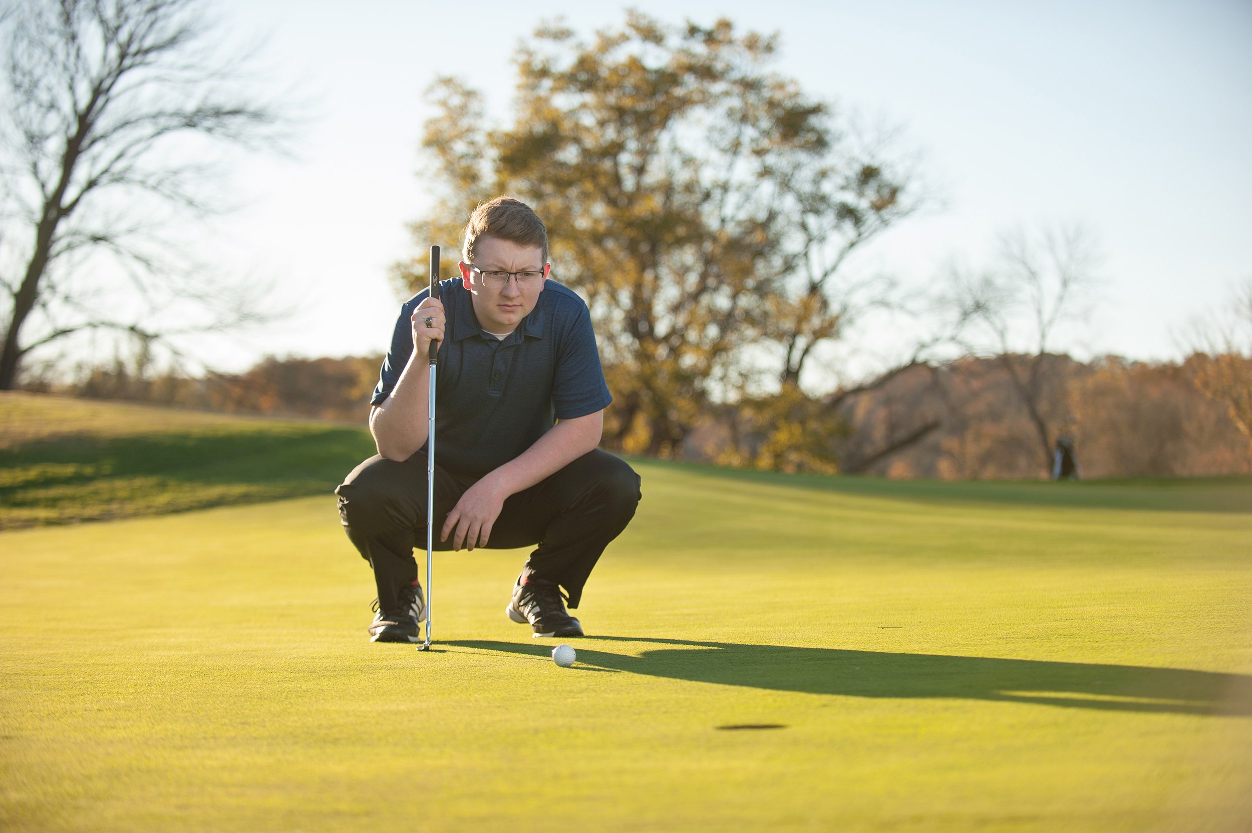 Senior guy golfer in blue shirt looking at his golf ball and the hole.