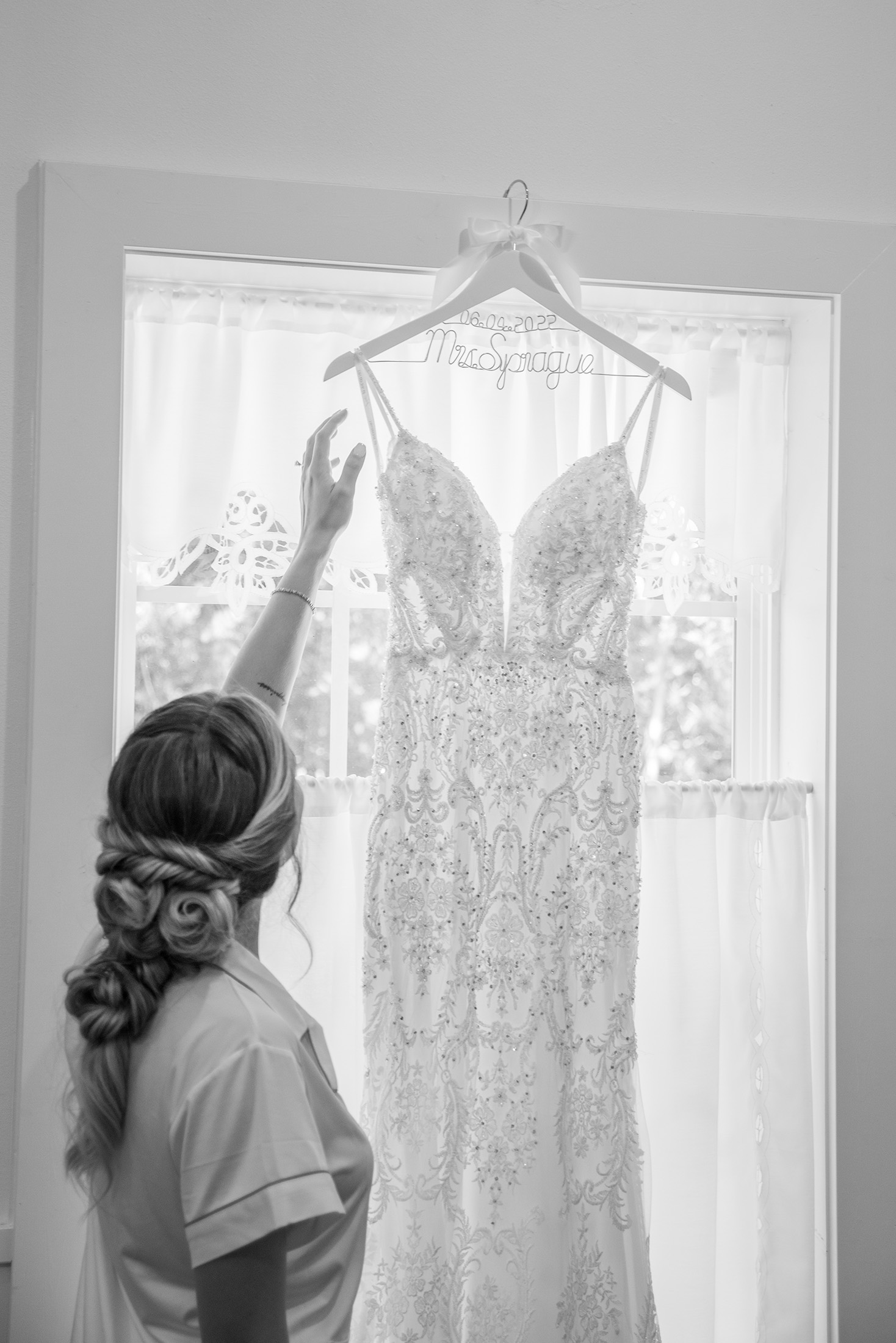 bride looking at boho lace wedding dress hanging in front of a window at Dooley's Chapel near Branson, MO.
