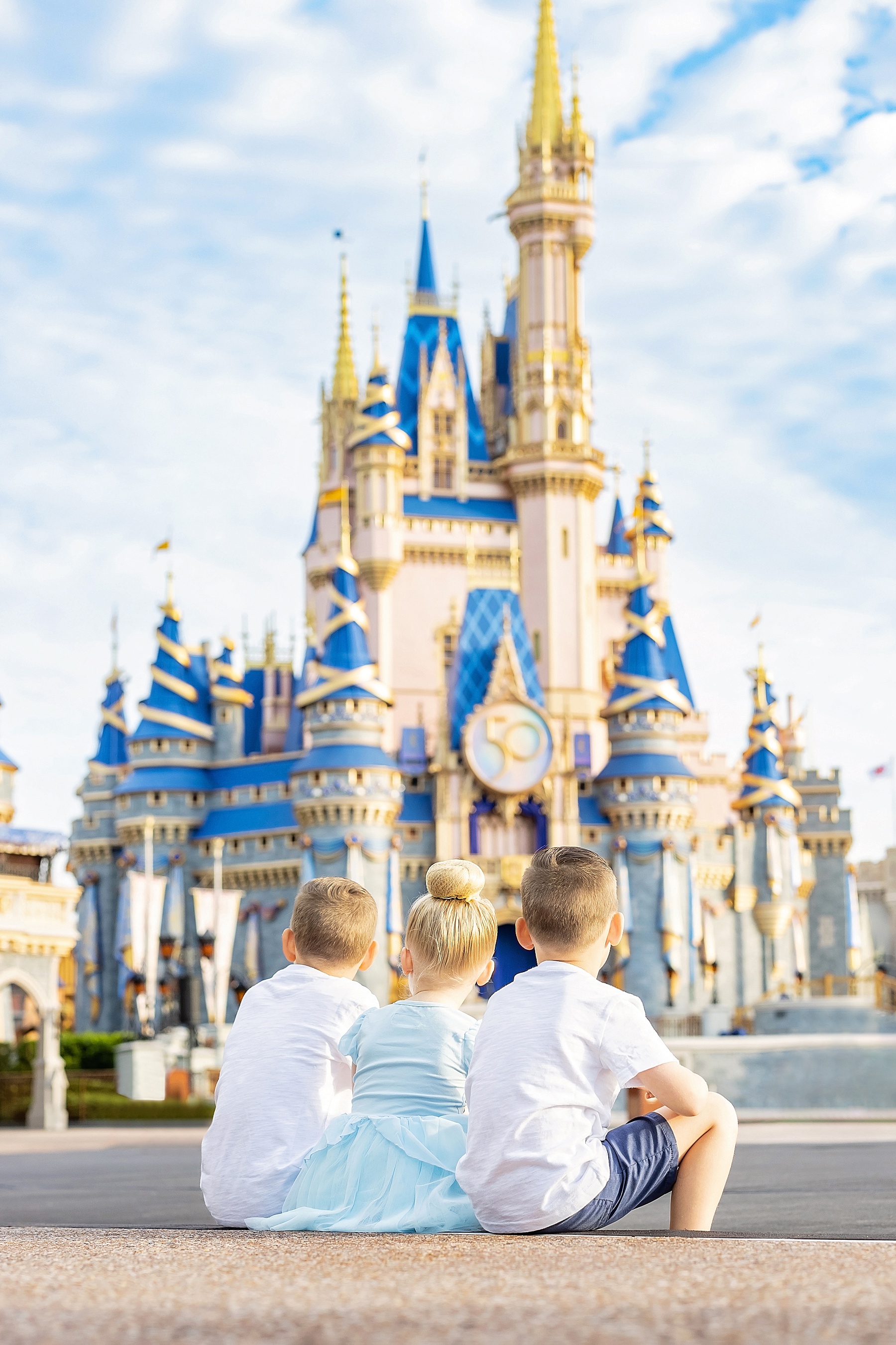 siblings sitting on pavement in front of Cinderella's Castle Walt Disney World Magic Kingdom