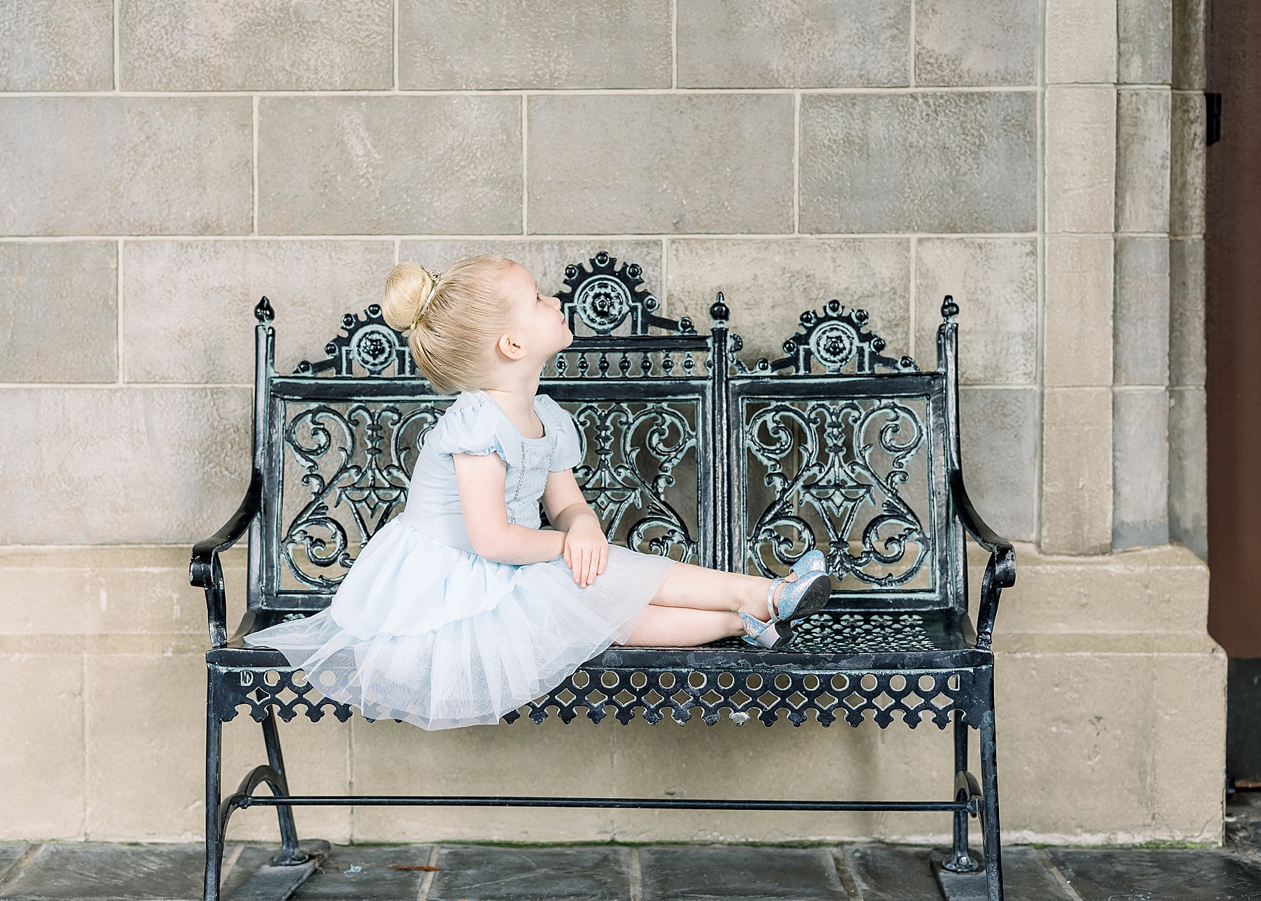 little girl in ballerina blue Cinderella dress on black iron bench
