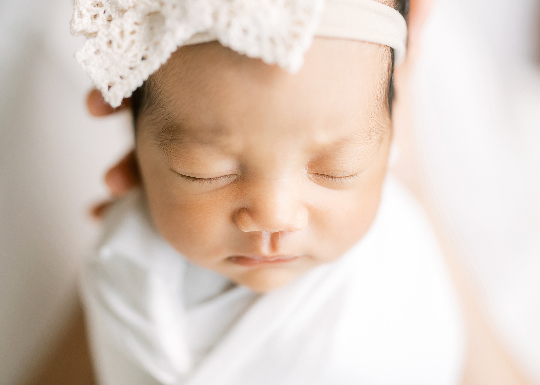 newborn baby girl wrapped in white swaddle and cream crochet bow