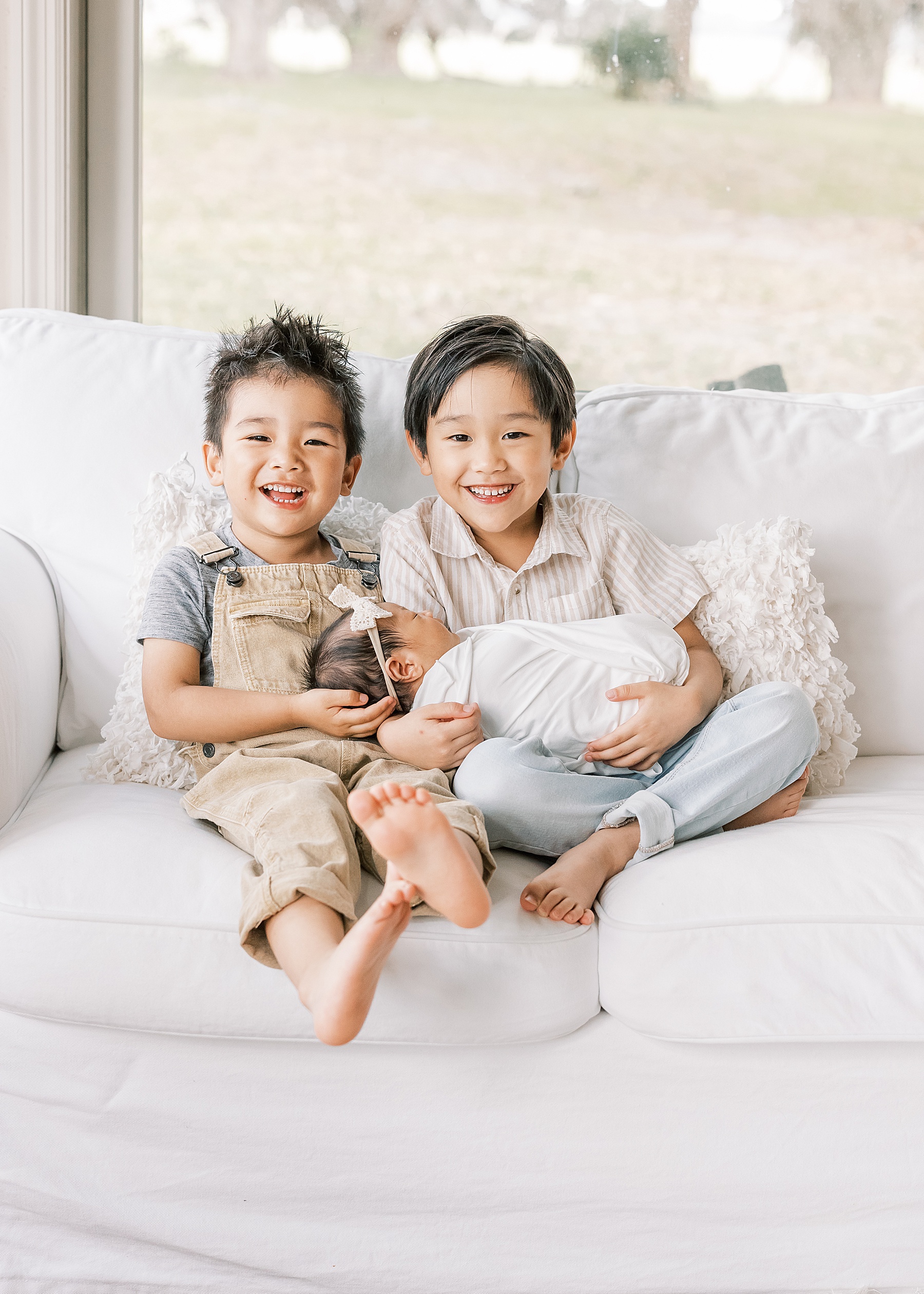 little asian boys holding newborn baby sister wrapped in white swaddle