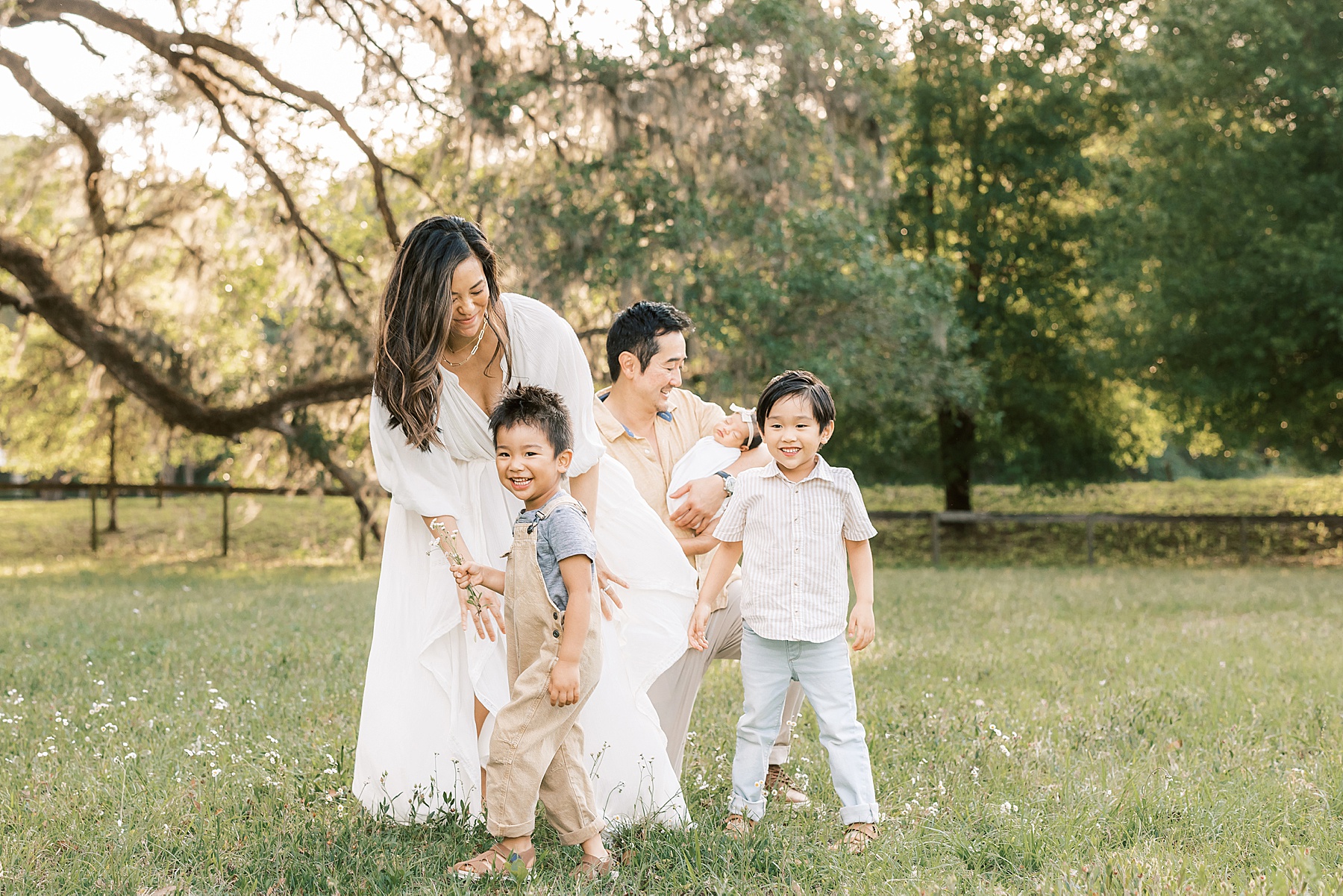 family playing in sunny flower field with newborn baby girl