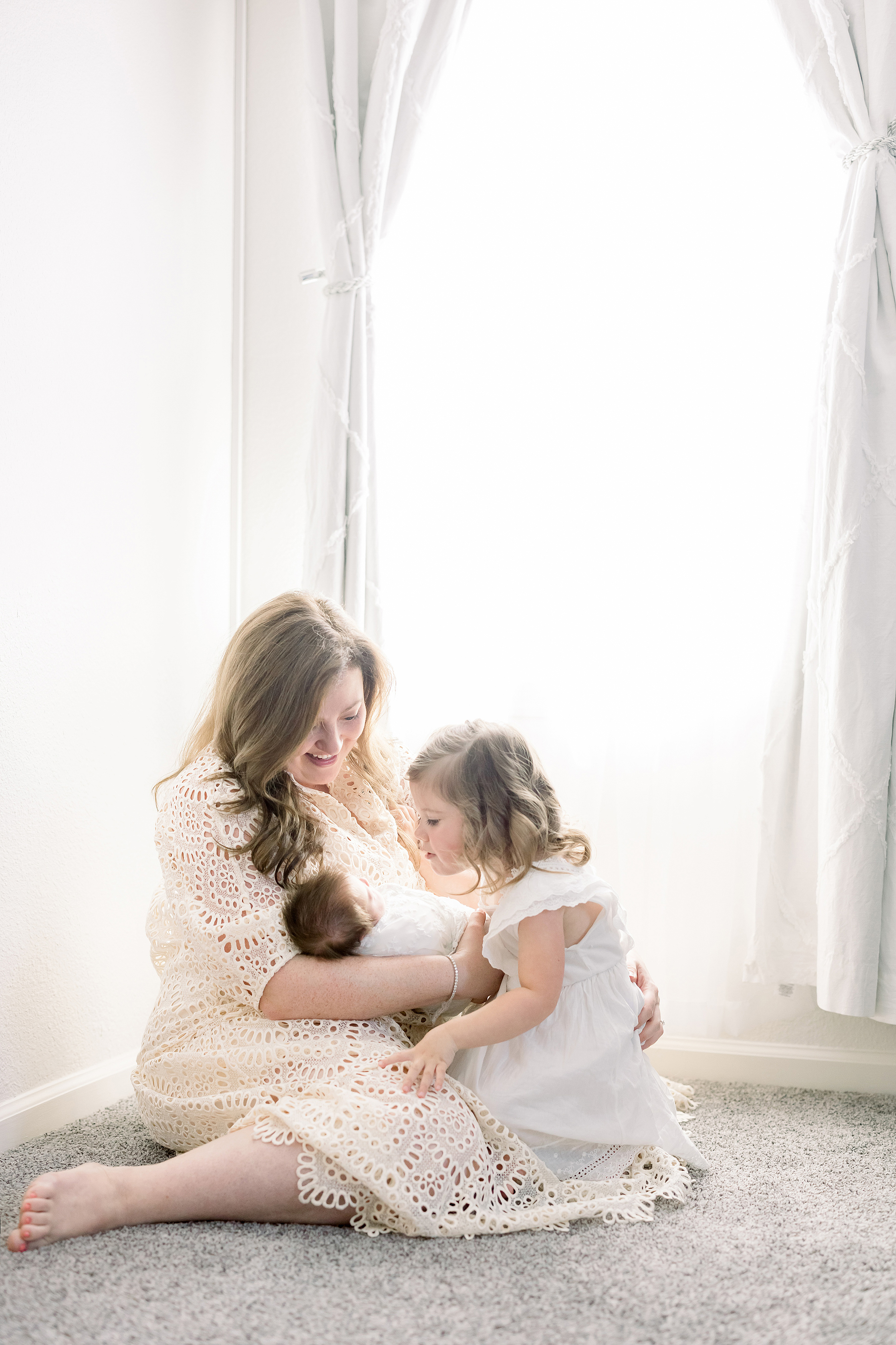 light and airy in home newborn portrait of woman with two daughters dressed in neutral clothing