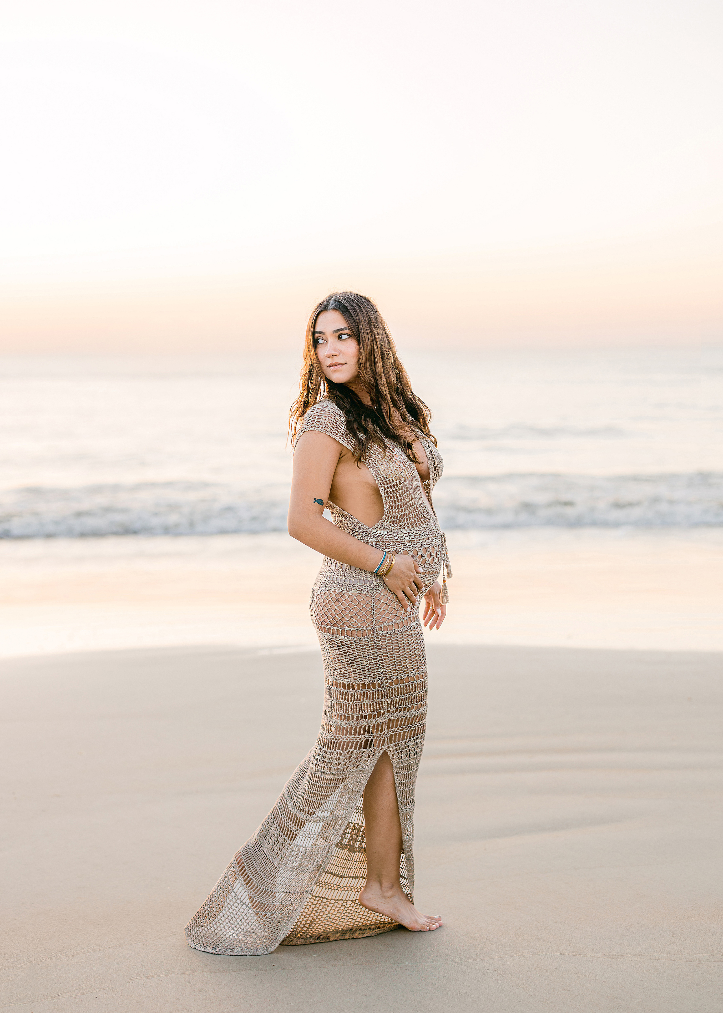 dark long haired woman walking on the sand in shimmery dress on the beach at sunrise