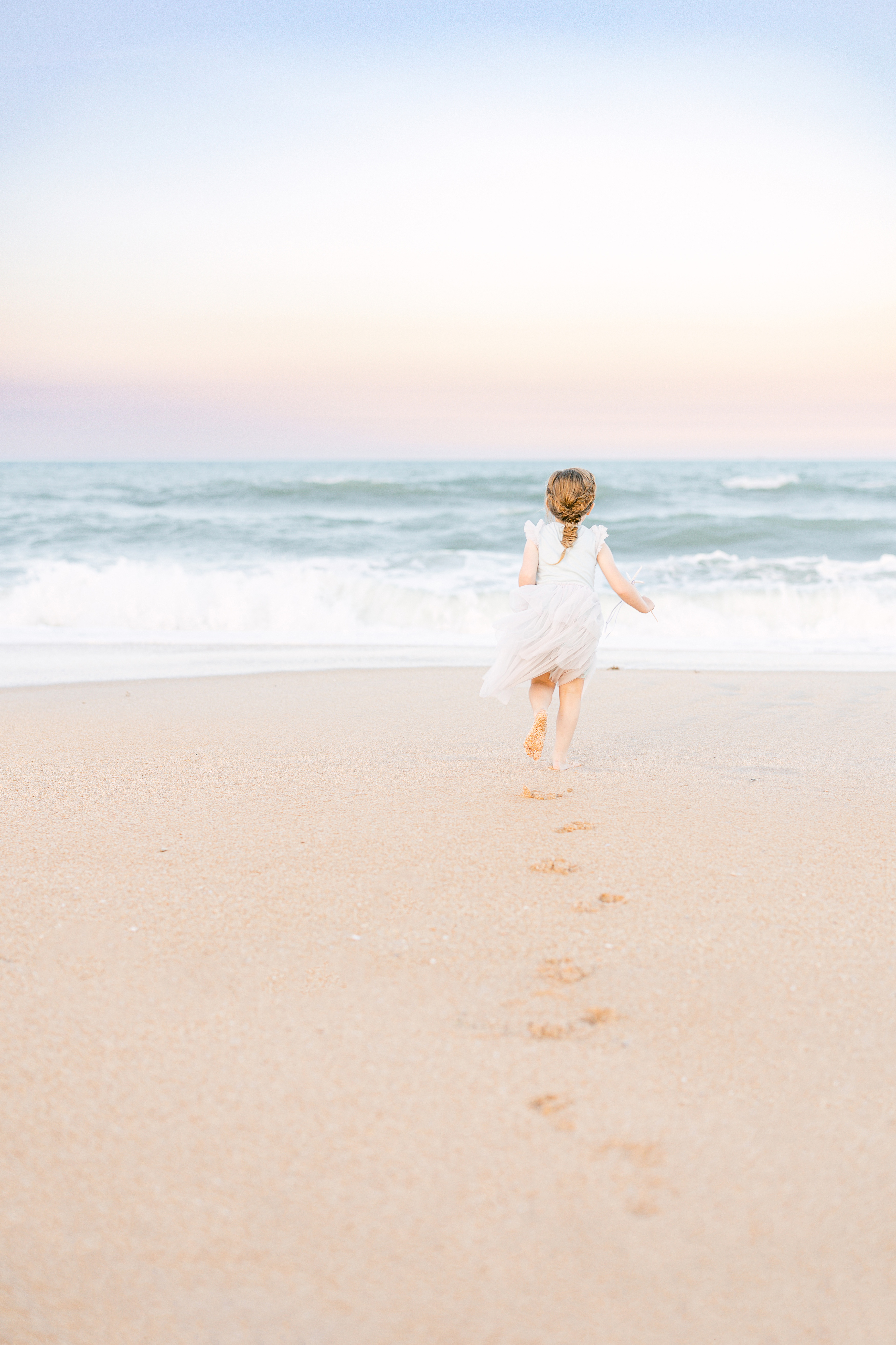 pastel beach portrait of a little girl running in the sand at sunset