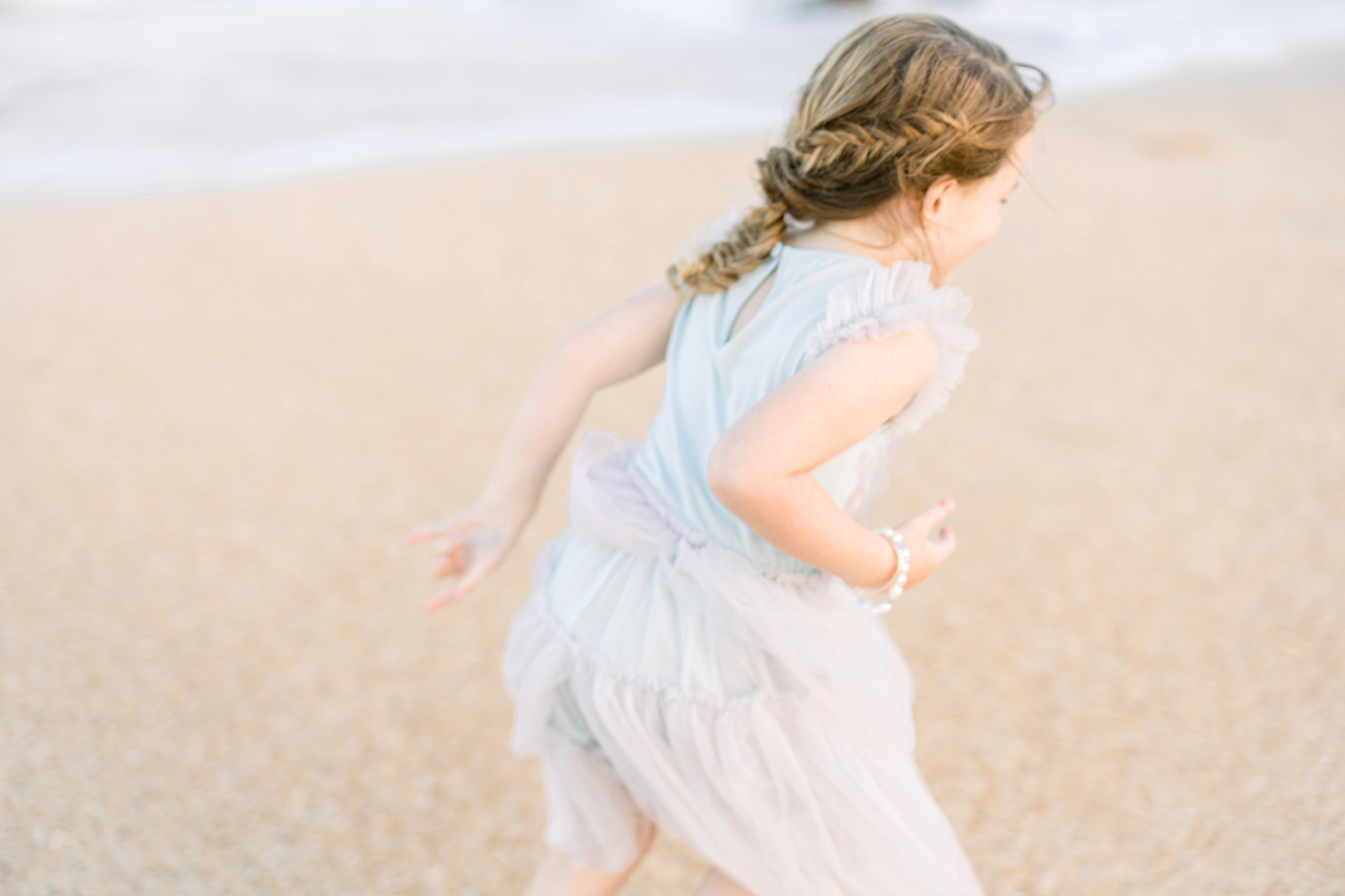 blurred image of little girl in pastel dress at the beach during a colorful sunset