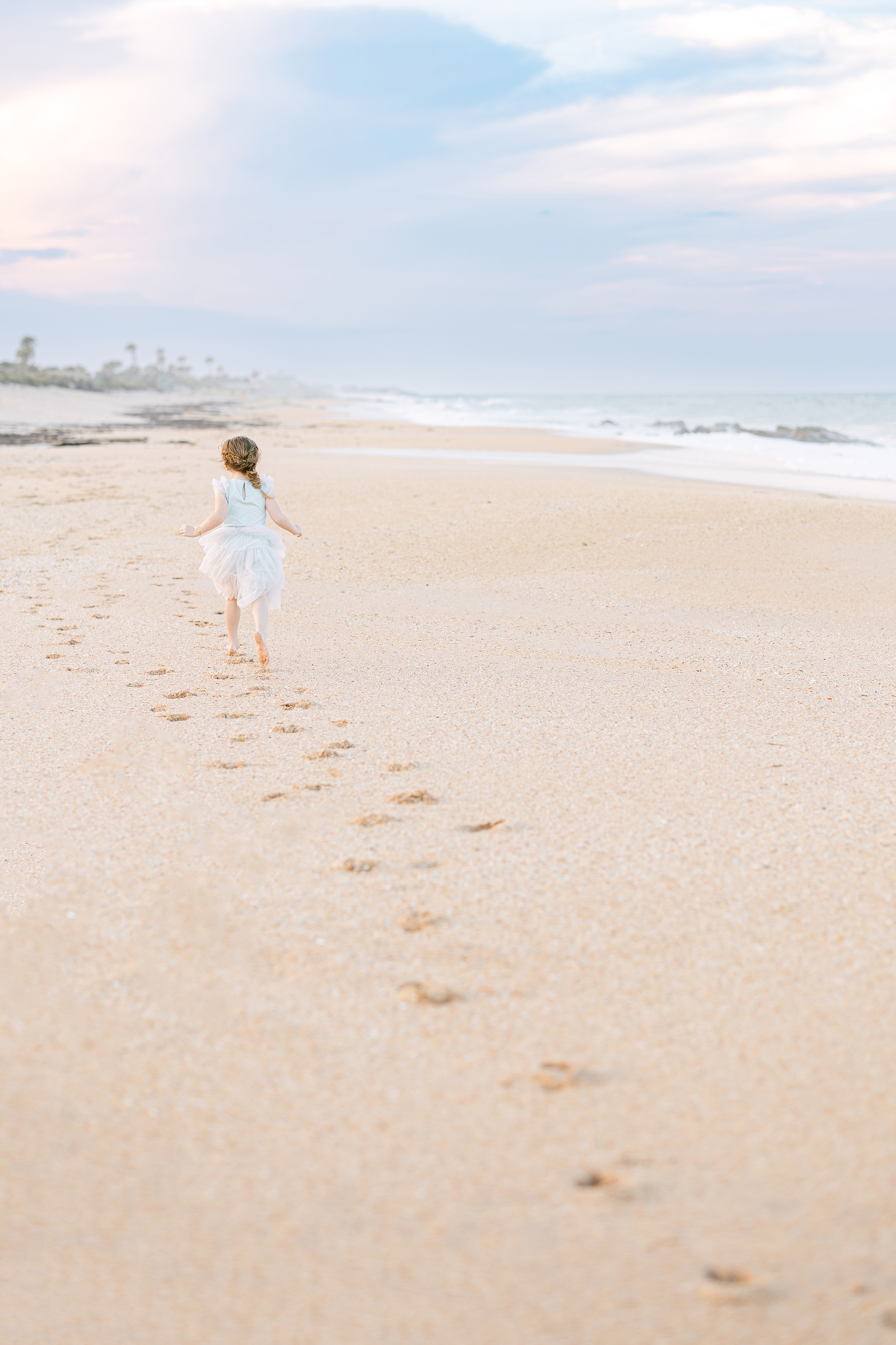 little girl in pastel mermaid dress running down the beach at sunset