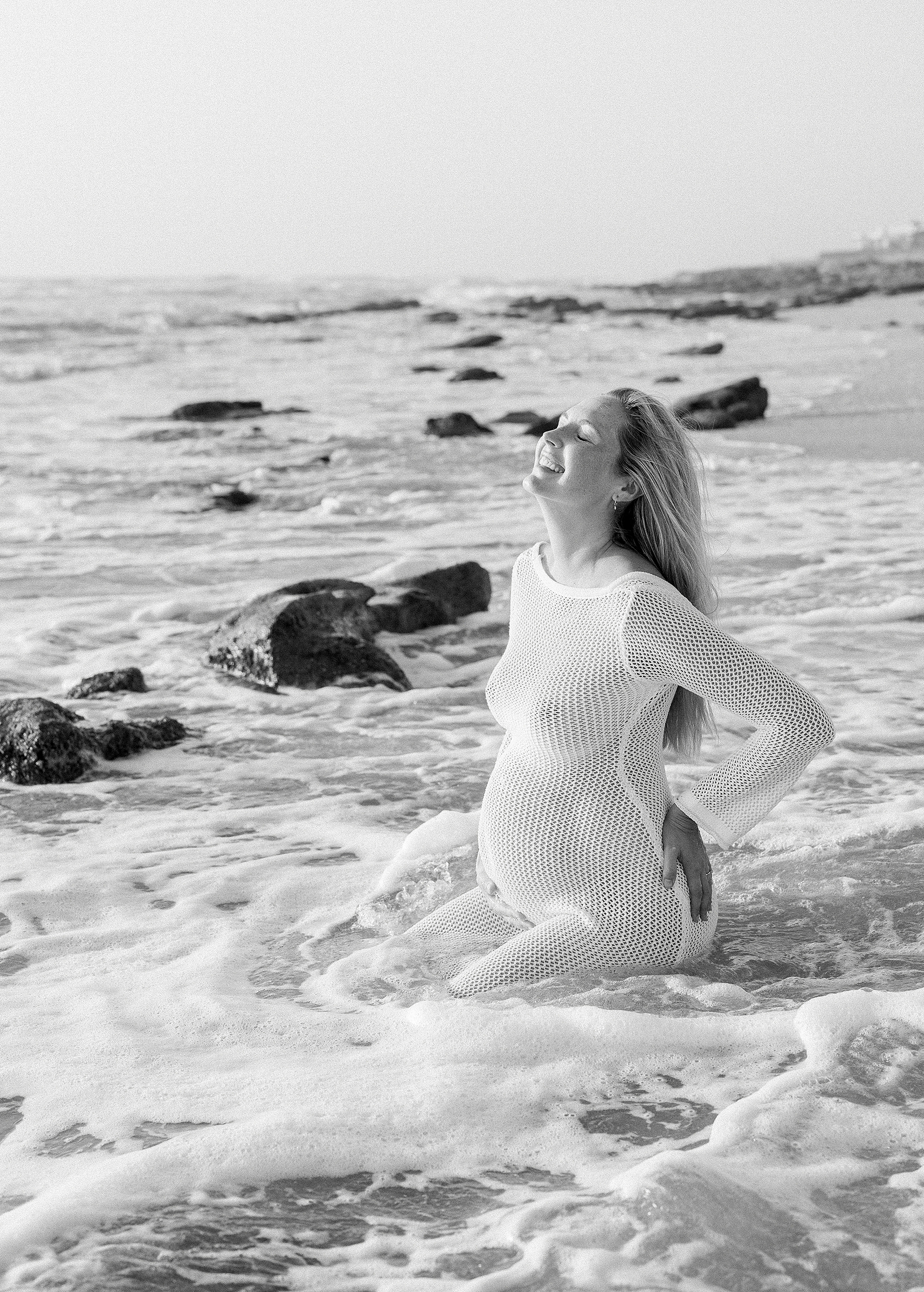 Black and white pregnancy portrait of woman sitting in the sand on St. Augustine Beach 